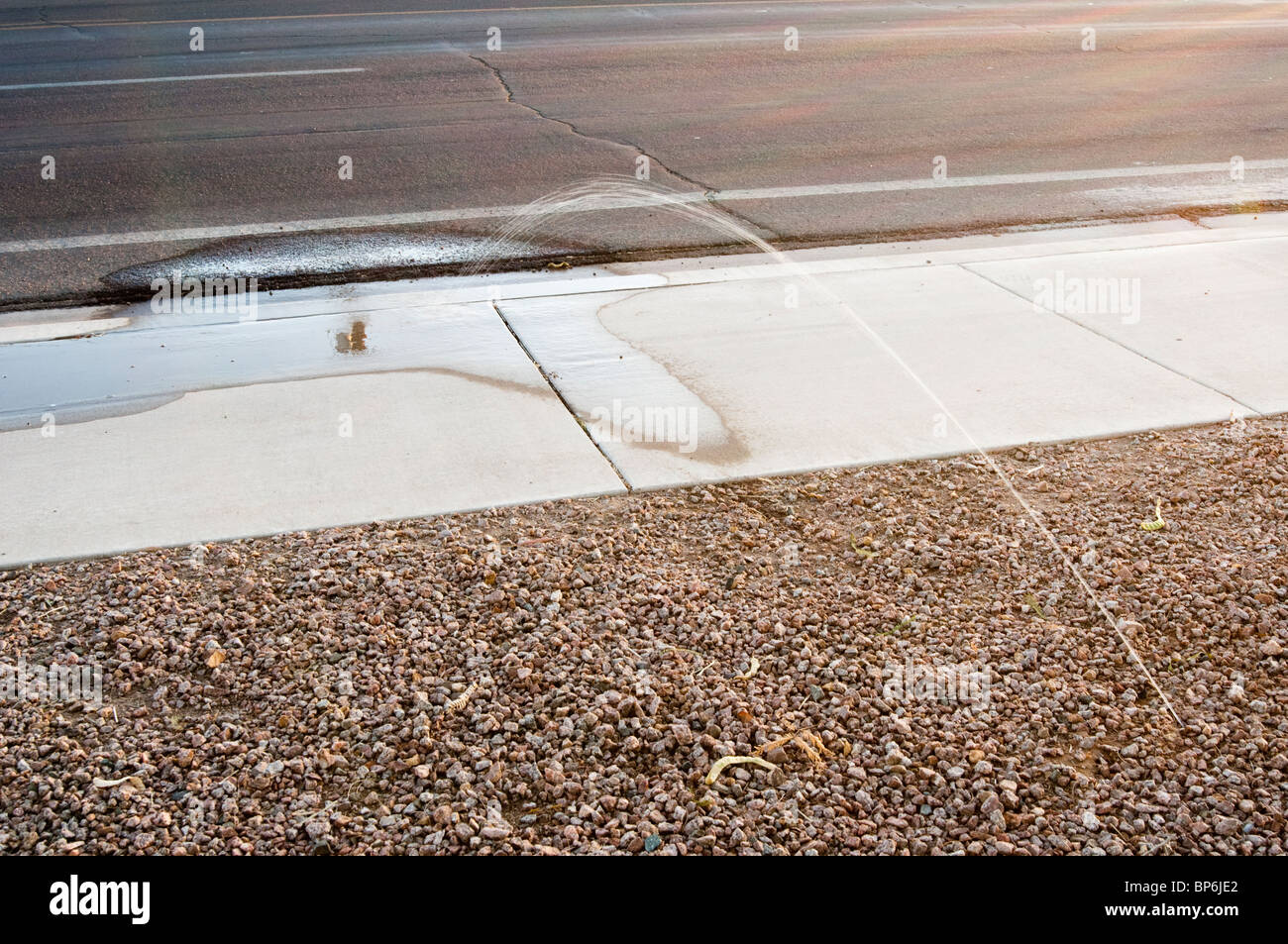 Un guasto antigoccia automatico sistema di irrigazione spruzza acqua in strada. Foto Stock