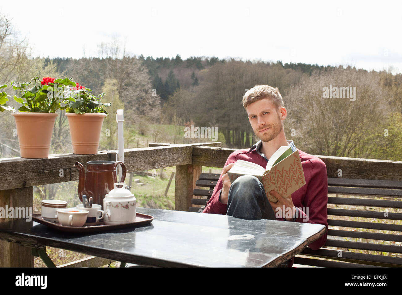 Un uomo seduto a un tavolo su un balcone la lettura Foto Stock