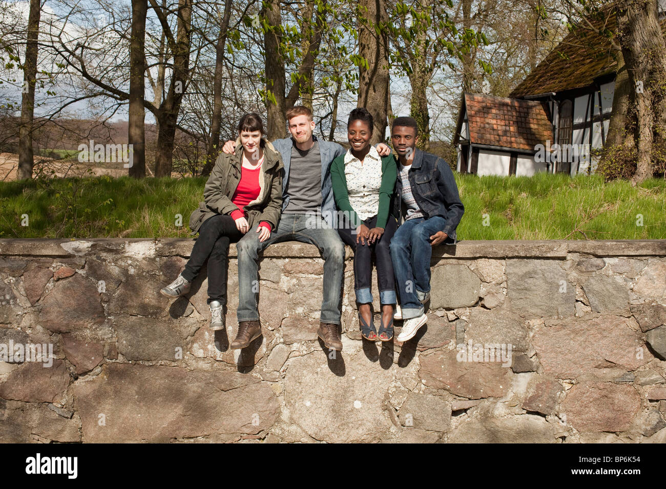 Quattro amici seduti su un muro di pietra Foto Stock