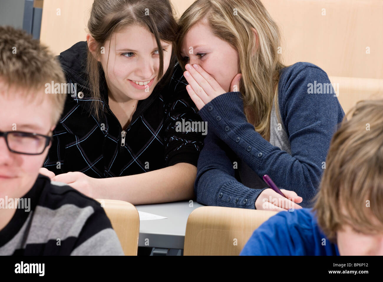 Due femmina di alta scuola gli studenti whispering in classe Foto Stock