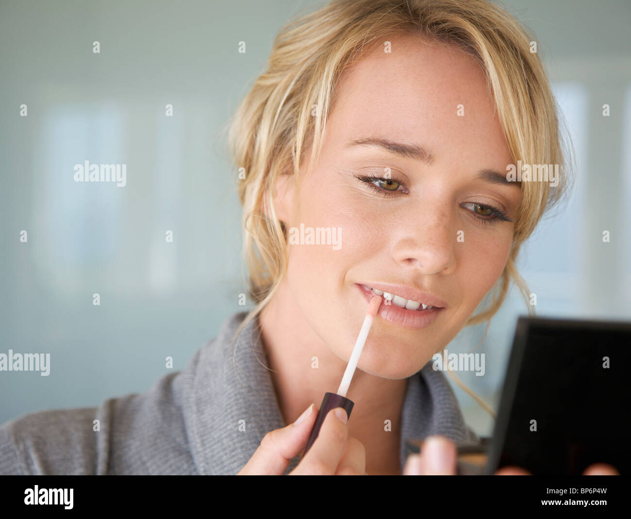 Una giovane donna applicando lip gloss Foto Stock
