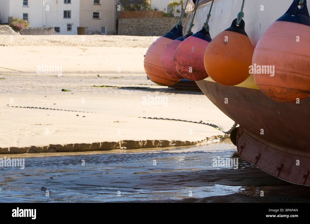 Parafanghi colorate sul lato di una barca da pesca a St Ives harbour con la bassa marea. Foto Stock