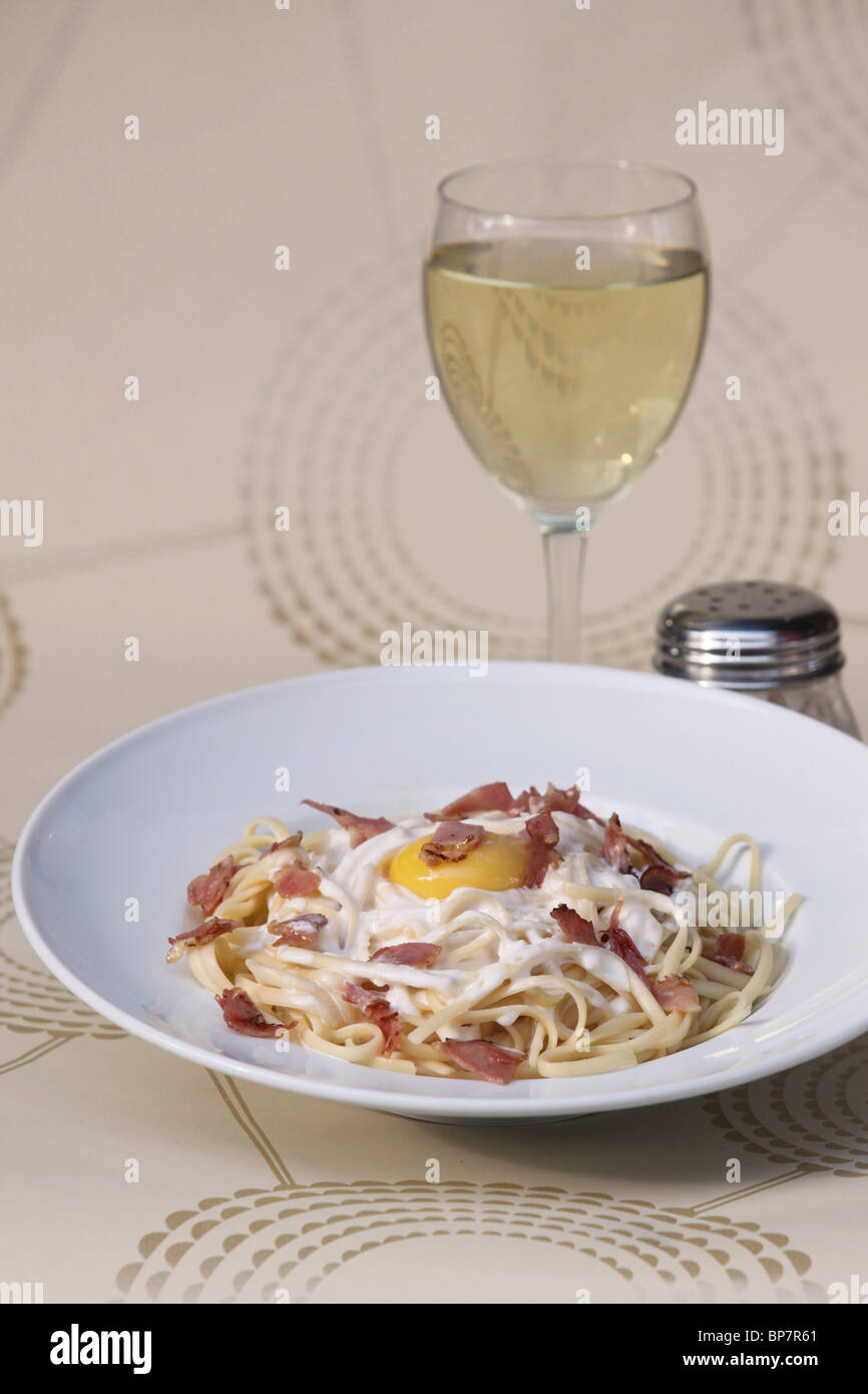 Piatto di linguine con pancetta e uova fritte e bicchiere di vino bianco Foto Stock