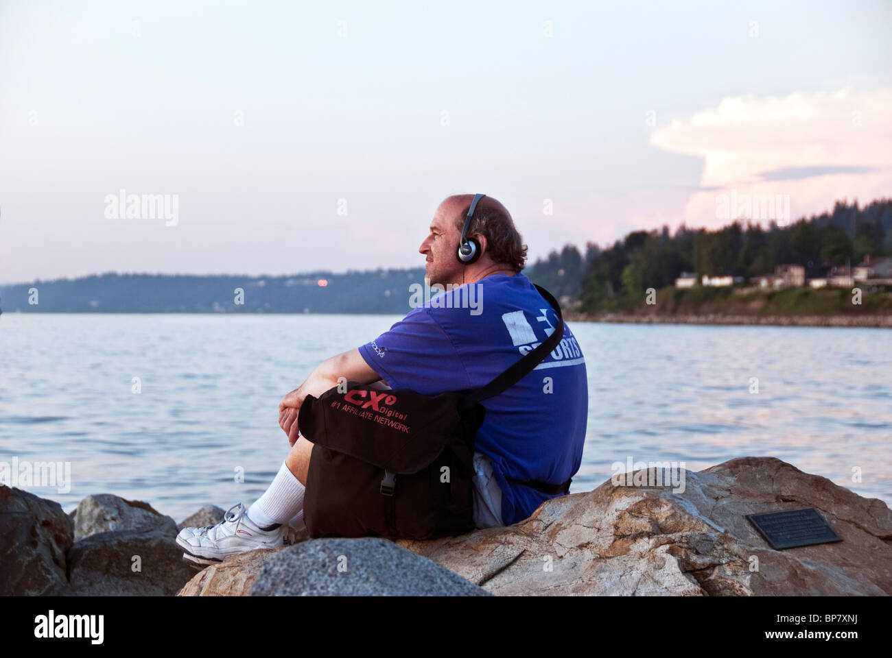 Rilassato felice uomo seduto sulle rocce al bordo delle acque al tramonto è uno studio di contentezza che si affacciava su Puget Sound Edmonds WA Foto Stock