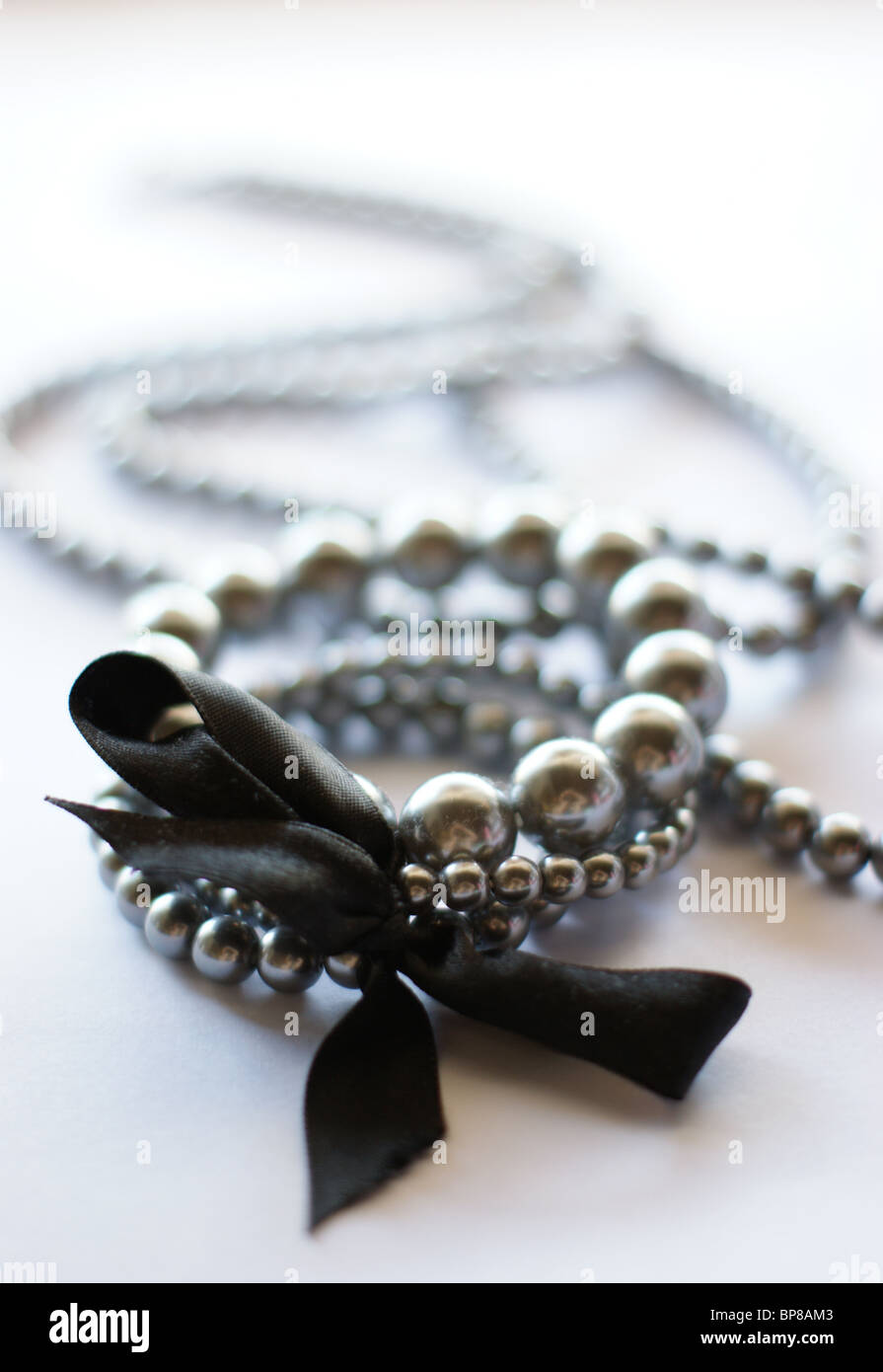 Un bracciale di tre fili di perle argento legati insieme con nastro nero e una collana di adattamento il fanalino di coda Foto Stock