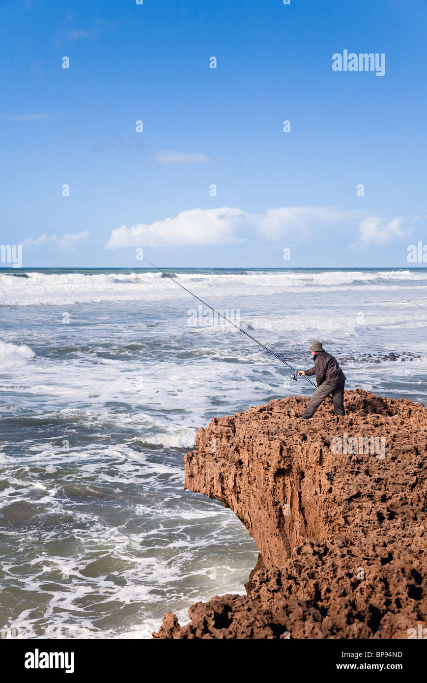 Pescatore che usa il rod tradizionale e la linea su scogliere aspre, Plage Aglou, Tiznit, costa atlantica, Marocco Foto Stock