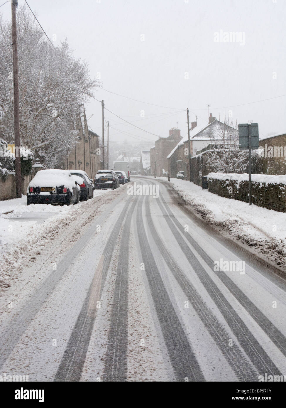 Neve spessa e tracce di auto su una strada in Cotswolds Foto Stock