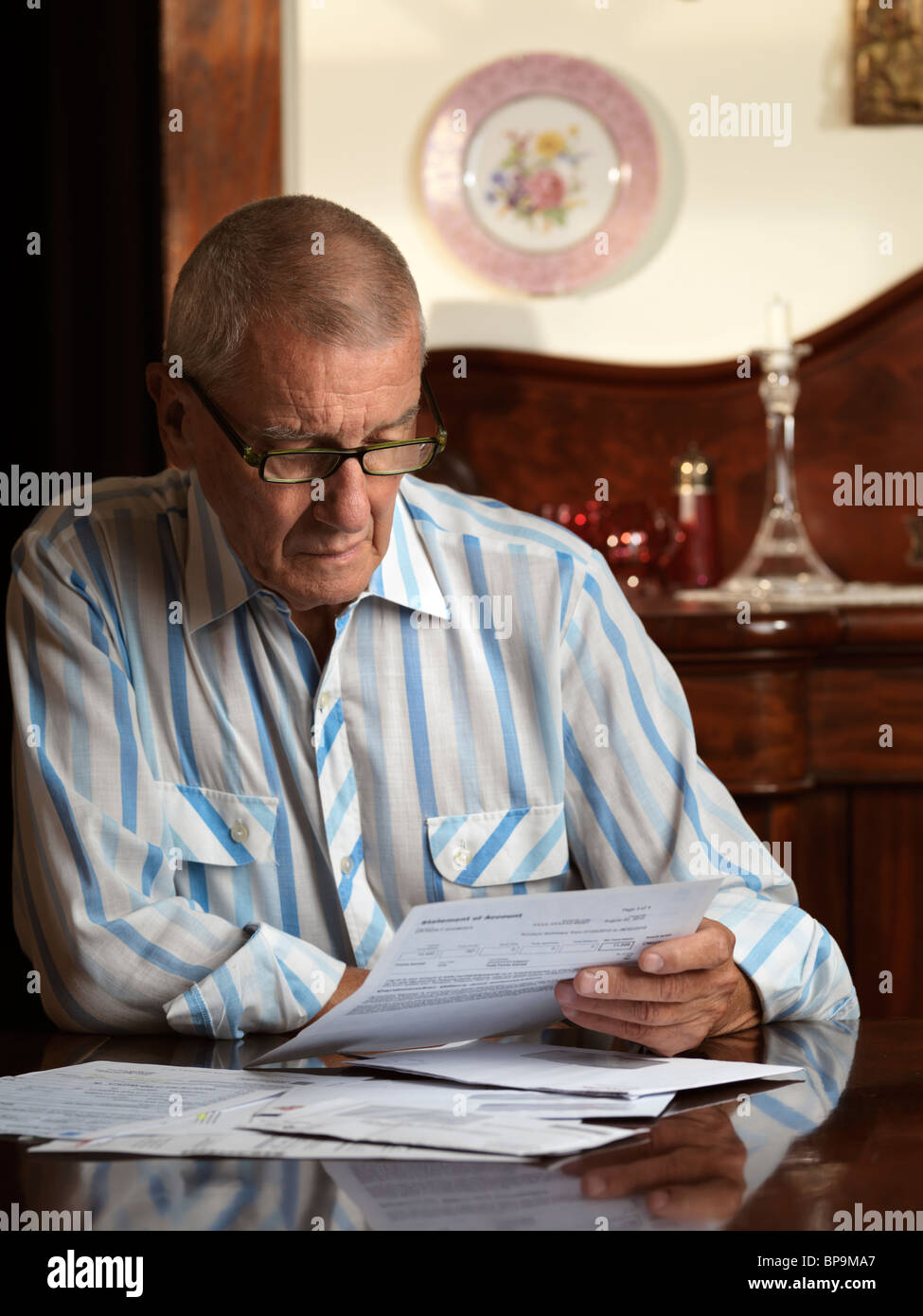 Uomo anziano seduto alla scrivania guardando attraverso le bollette Foto Stock