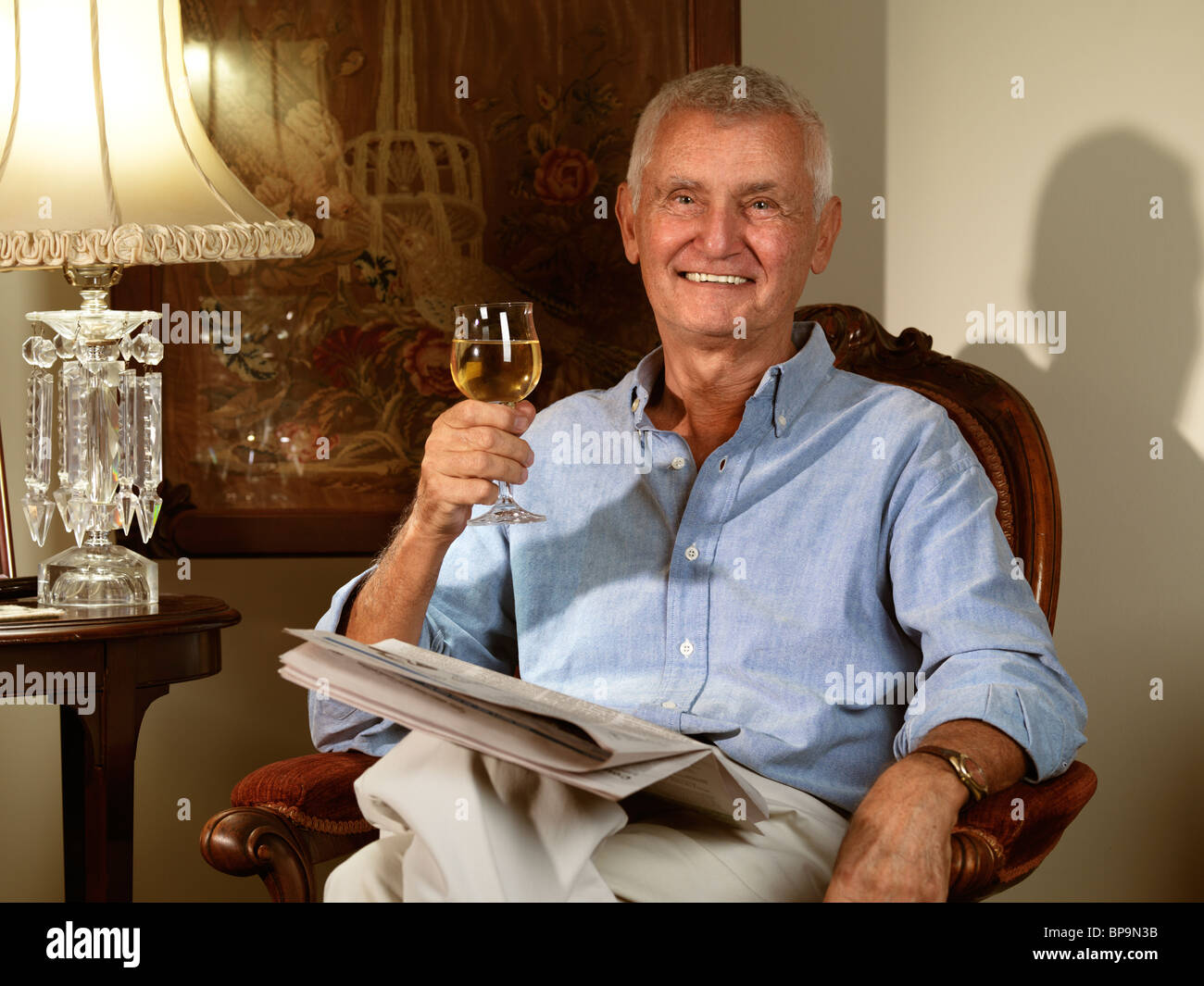 Anziani uomo seduto in una sedia con un quotidiano e un bicchiere di vino in mano Foto Stock