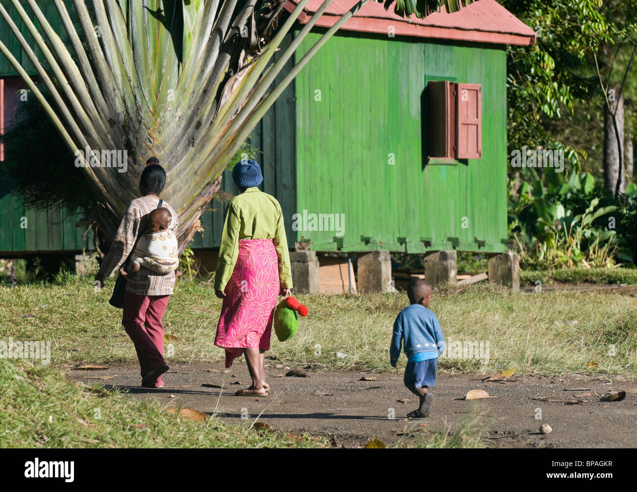 Le donne con bambini passano da una zona rurale casa in legno a Ranomafana, Madagascar Foto Stock