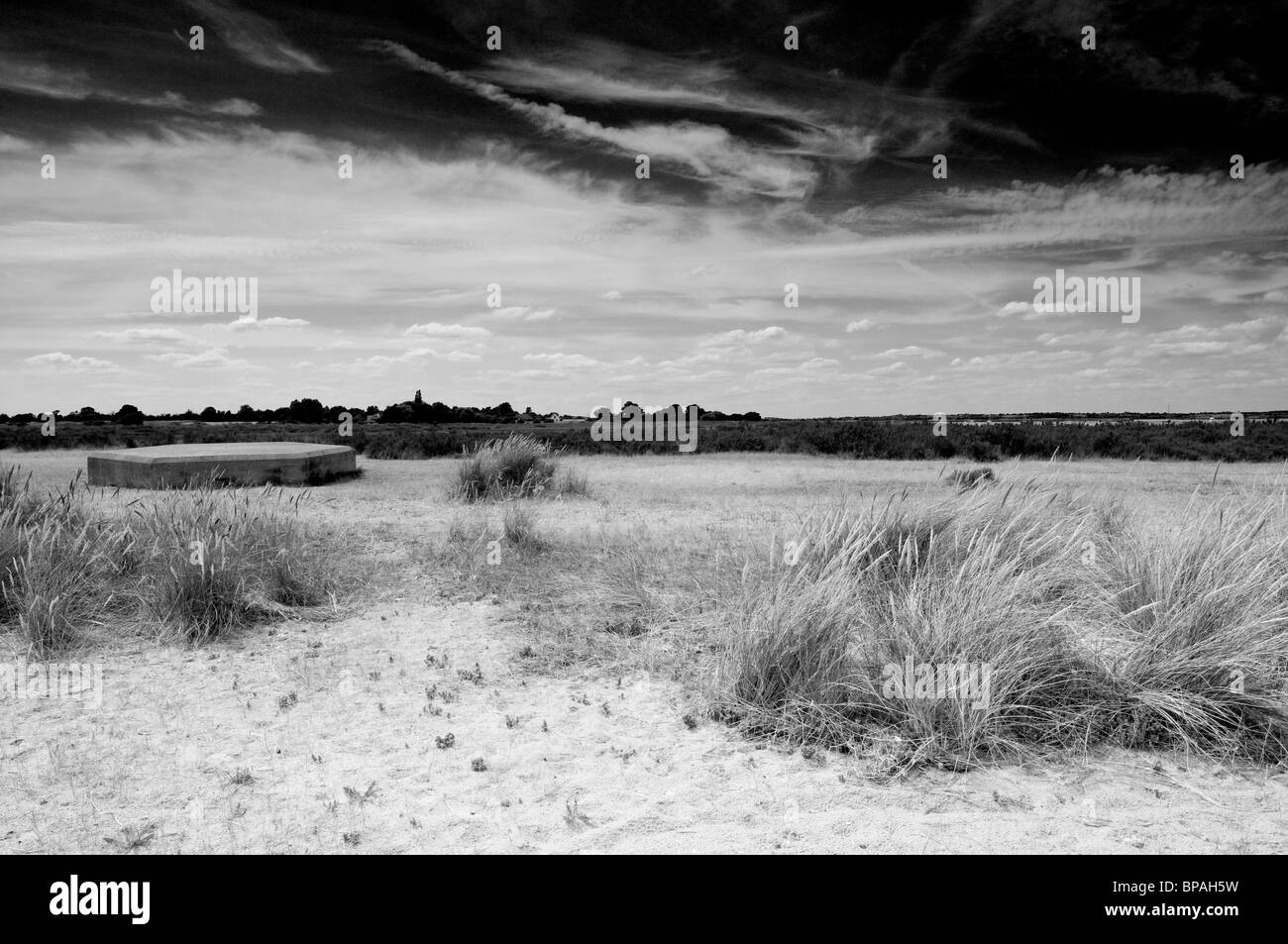 Una scatola di pillole sulla spiaggia nelle zone costiere Essex. Sabbia e erba in primo piano e uno scuro, drammatico, cielo nuvoloso. In bianco e nero. Foto Stock