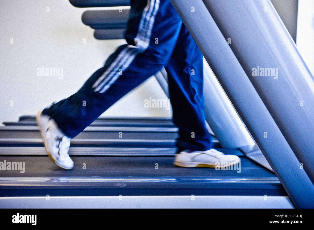 Gambe non identificabili che indossano fondi sciolti da jogging che corrono su un tapis roulant in una palestra. Foto Stock