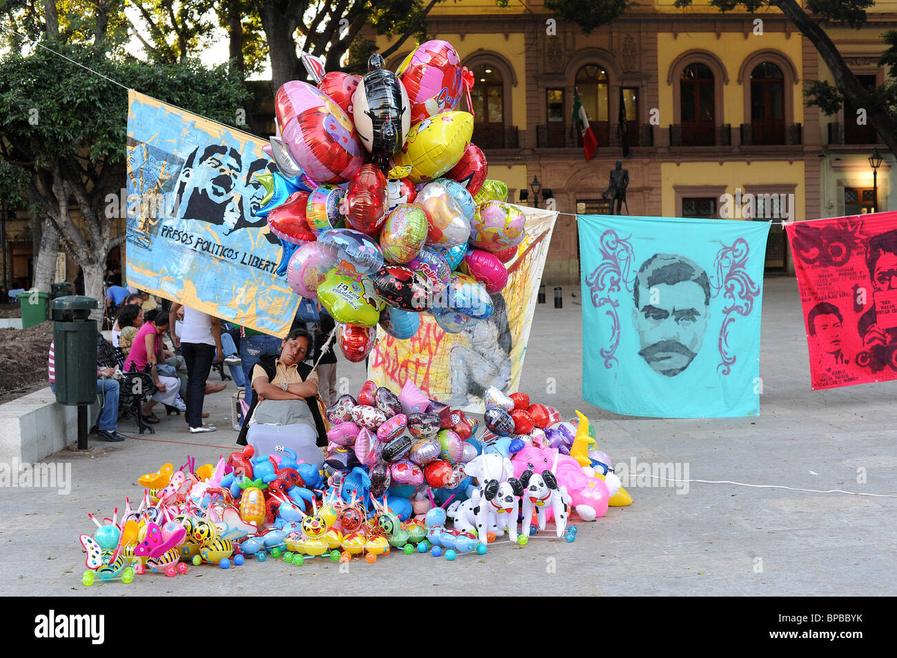 Il fornitore si addormenta in Zocola, il centro sociale di Oaxaca, Messico, mentre la vendita di vivacemente di palloncini colorati e giocattoli. Foto Stock