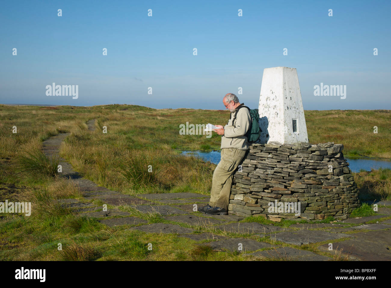 Walker in appoggio contro il punto di innesco sul Black Hill, Pennine Way, West Yorkshire, Inghilterra, Regno Unito Foto Stock