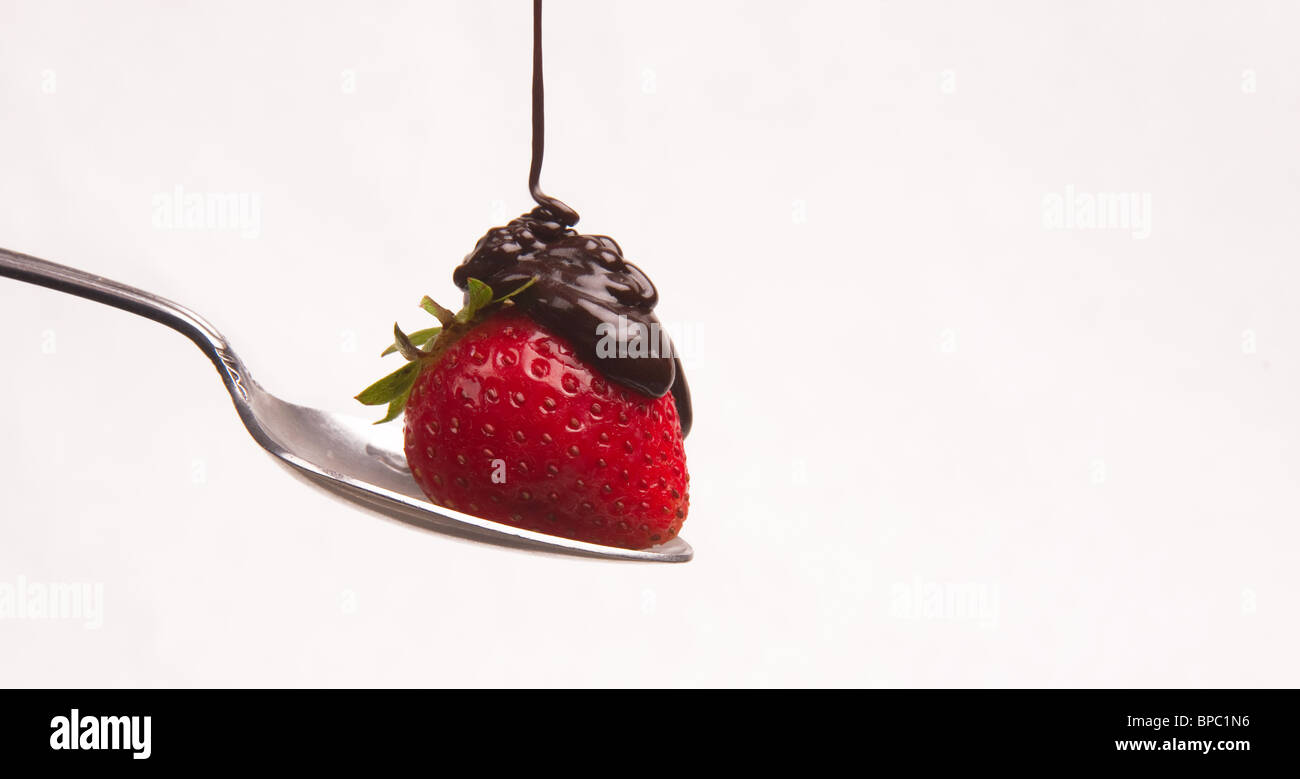Sciroppo al cioccolato gocce su una fragola seduto su un cucchiaio isolato su bianco Foto Stock