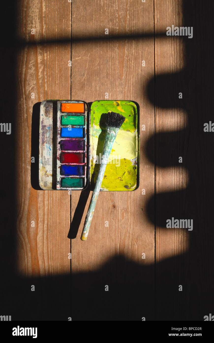 Usato antichi artisti paintbox acquerello e spazzola di vernice su di una superficie di legno con profonde ombre sagomato. Foto Stock Usato antichi artisti paintbox acquerello e spazzola di vernice su di una superficie di legno con profonde ombre sagomato. Foto Stock