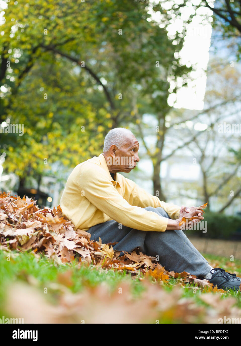 Senior uomo si siede in foglie di autunno nel parco Foto Stock