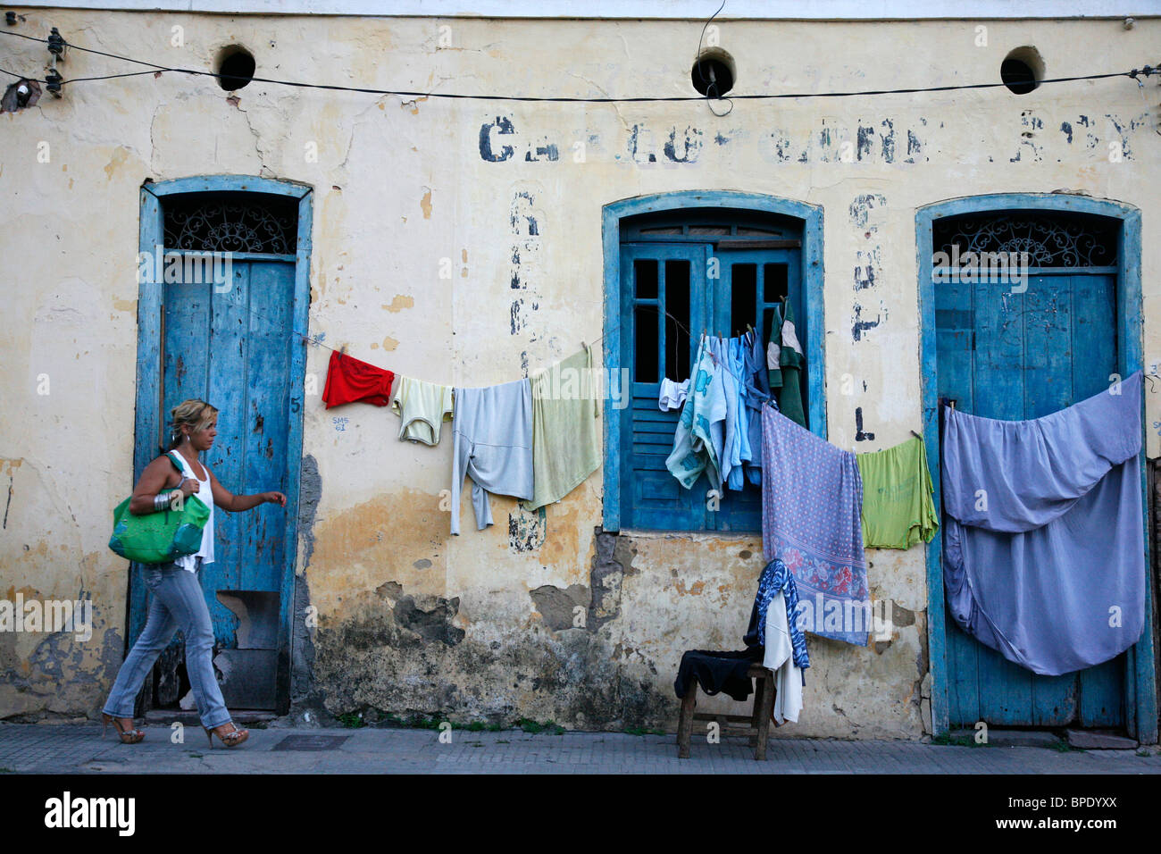 Donna che cammina da un vecchio edificio con servizio lavanderia appeso, Cachoeira, Bahia, Brasile. Foto Stock