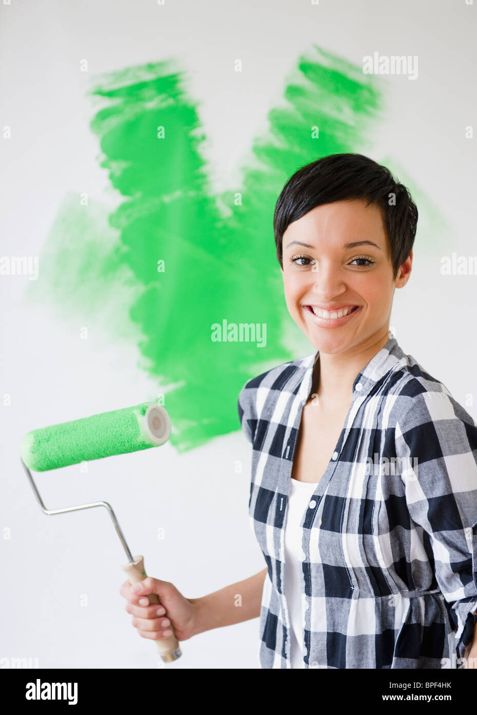 Razza mista donna che mantiene il rullo di vernice con della vernice verde Foto Stock