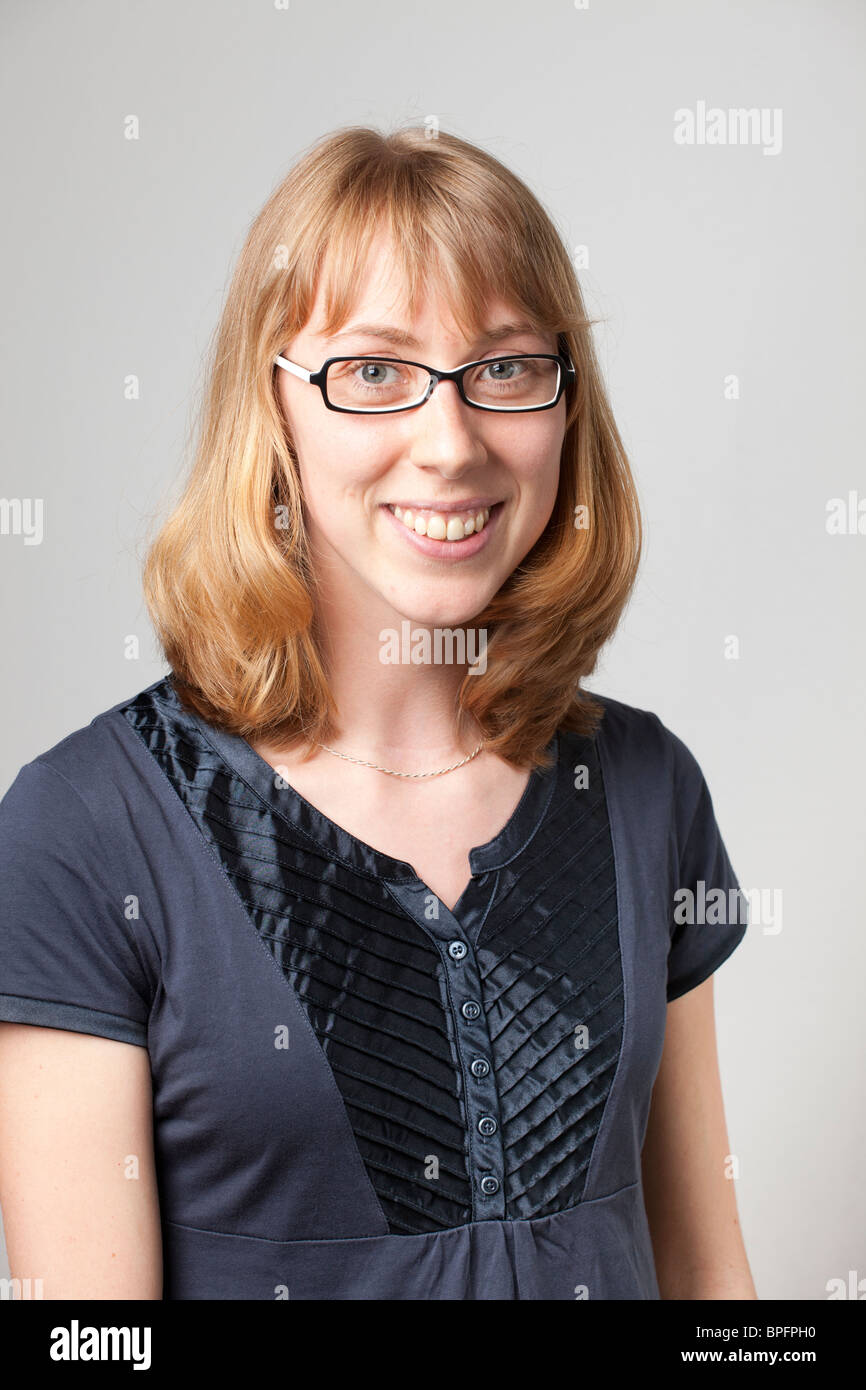 Donna sorridente con occhiali e capelli biondi corti, con la parte superiore blu navy, che guarda la fotocamera in uno studio fotografico. Foto Stock