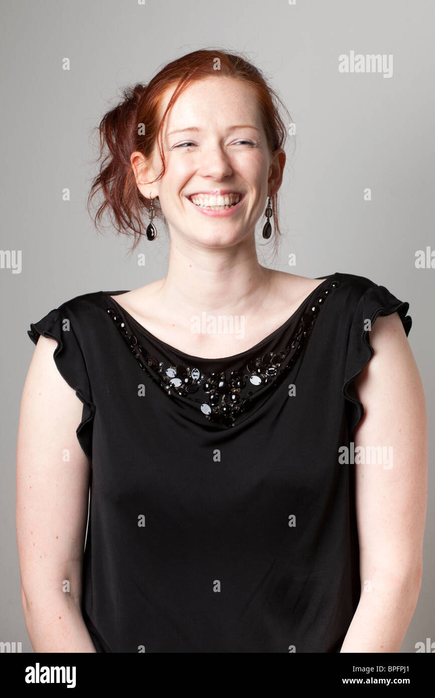 Donna sorridente dai capelli rossi con un top nero con paillettes, che guarda fuori dalla fotocamera e indossa orecchini pendenti. Foto Stock