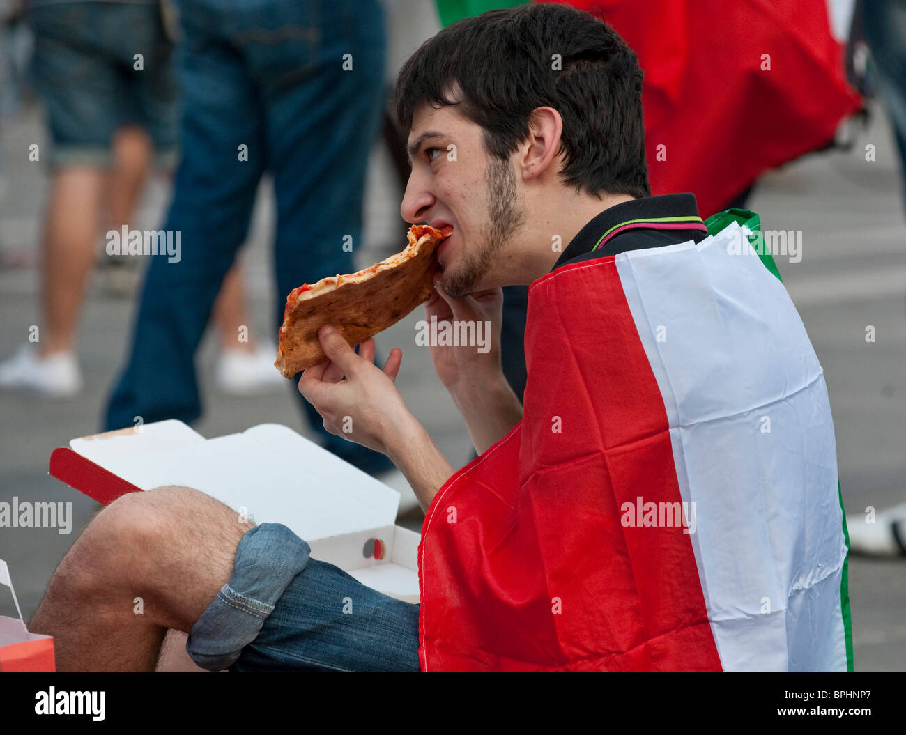 Un appassionato di calcio mangia la pizza durante la visione di un Italia 's gioco di squadra sul grande schermo in Piazza del Duomo Milano Italia Foto Stock