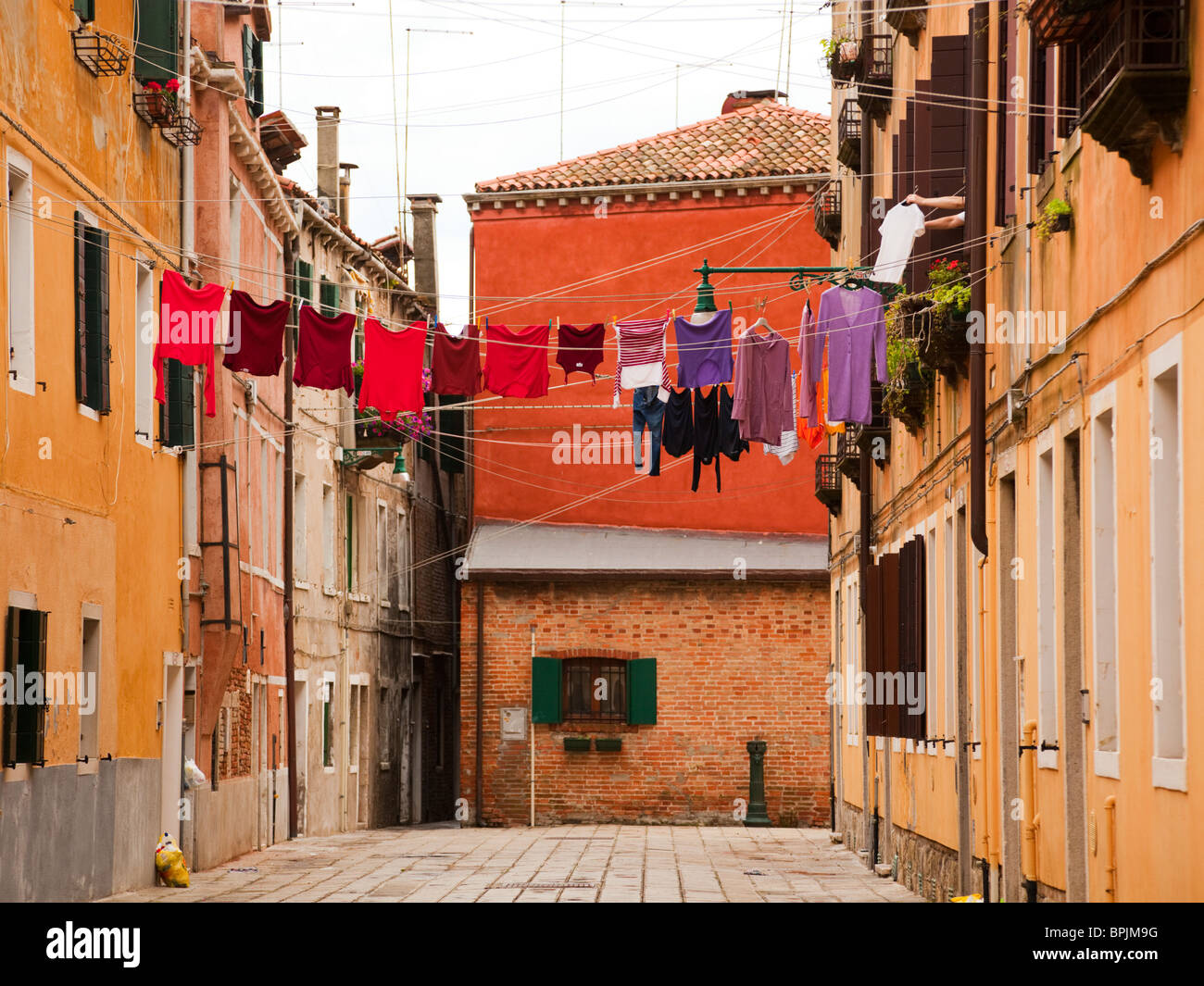 Cortile sul retro di casa Venezia, rosso e viola stendibiancheria su vestiti-linea, donna appesa una camicia dalla sua finestra Foto Stock