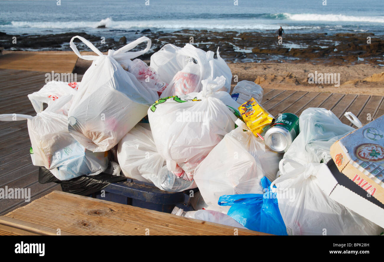 Traboccante bidone con ruote e scatola pizza sulla spiaggia in Spagna. Surfer provenienti al di fuori dell'acqua in background Foto Stock