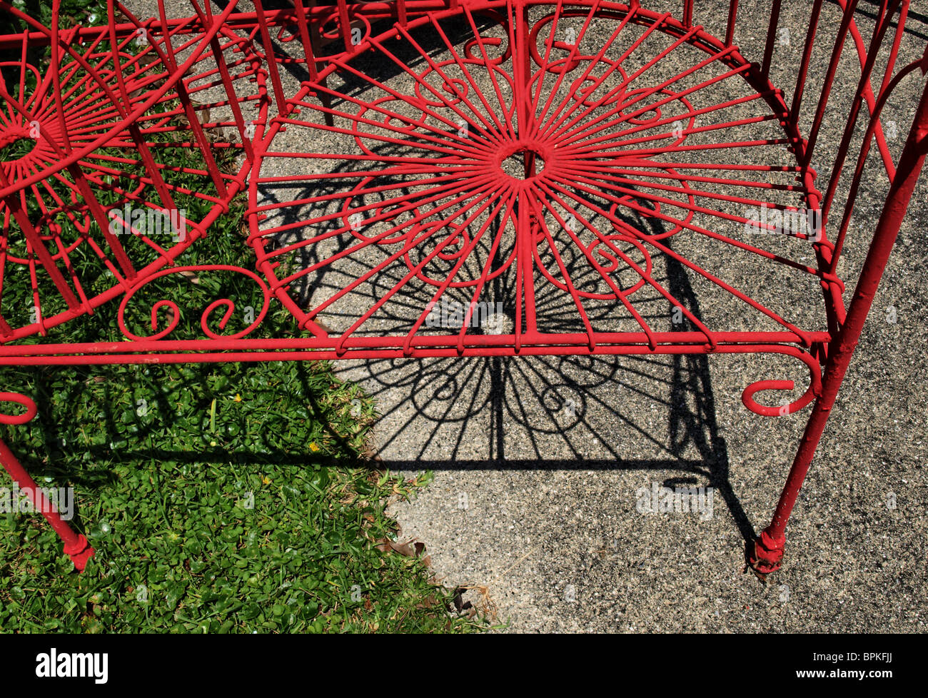 Dipinto di rosso sedia metallo parziale con ombre ornato di opere di filo a terra Foto Stock