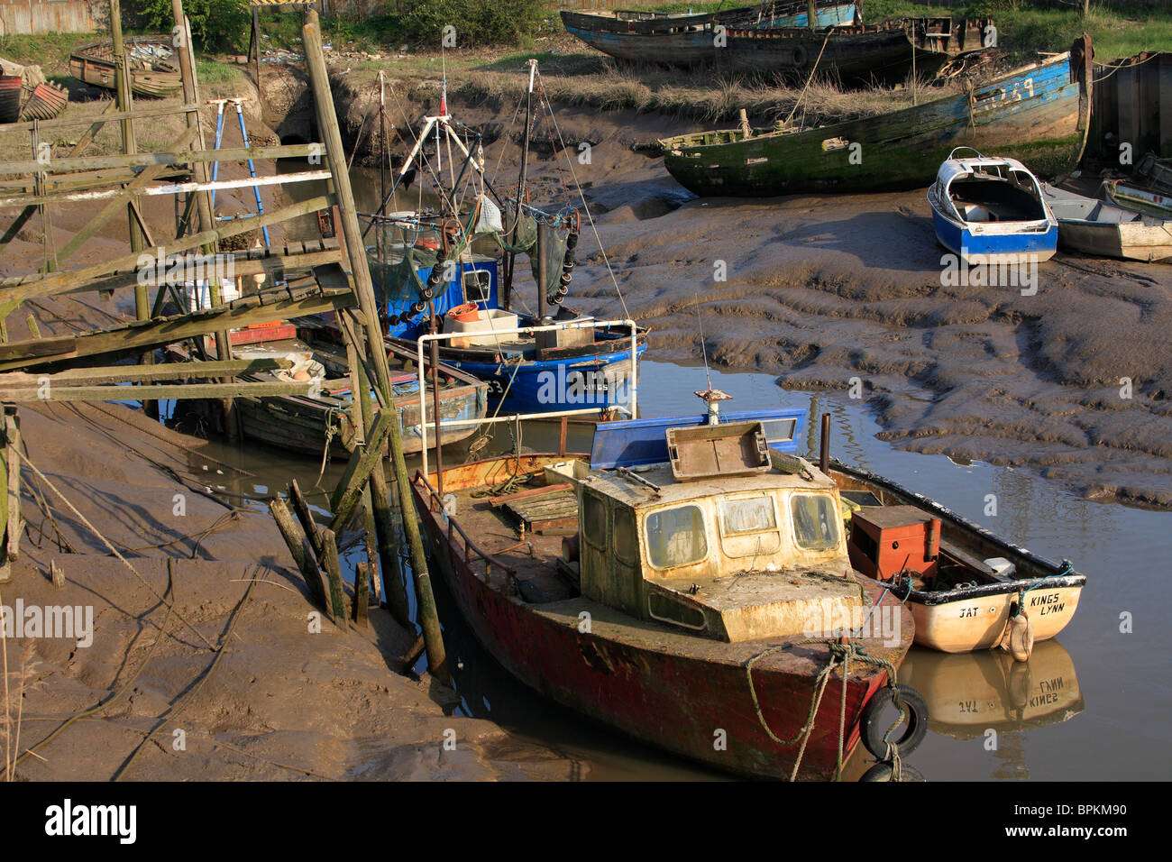 Vecchie barche da pesca in un ormeggio fangoso adiacente ad un pontone traballanti in sera sunshine, Kings Lynn, Norfolk Foto Stock