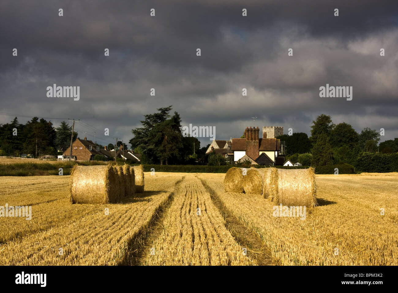 La raccolta di paglia lascia dietro di sé le balle insieme contro un cielo che consente a Sun di rompere attraverso intermitently Foto Stock