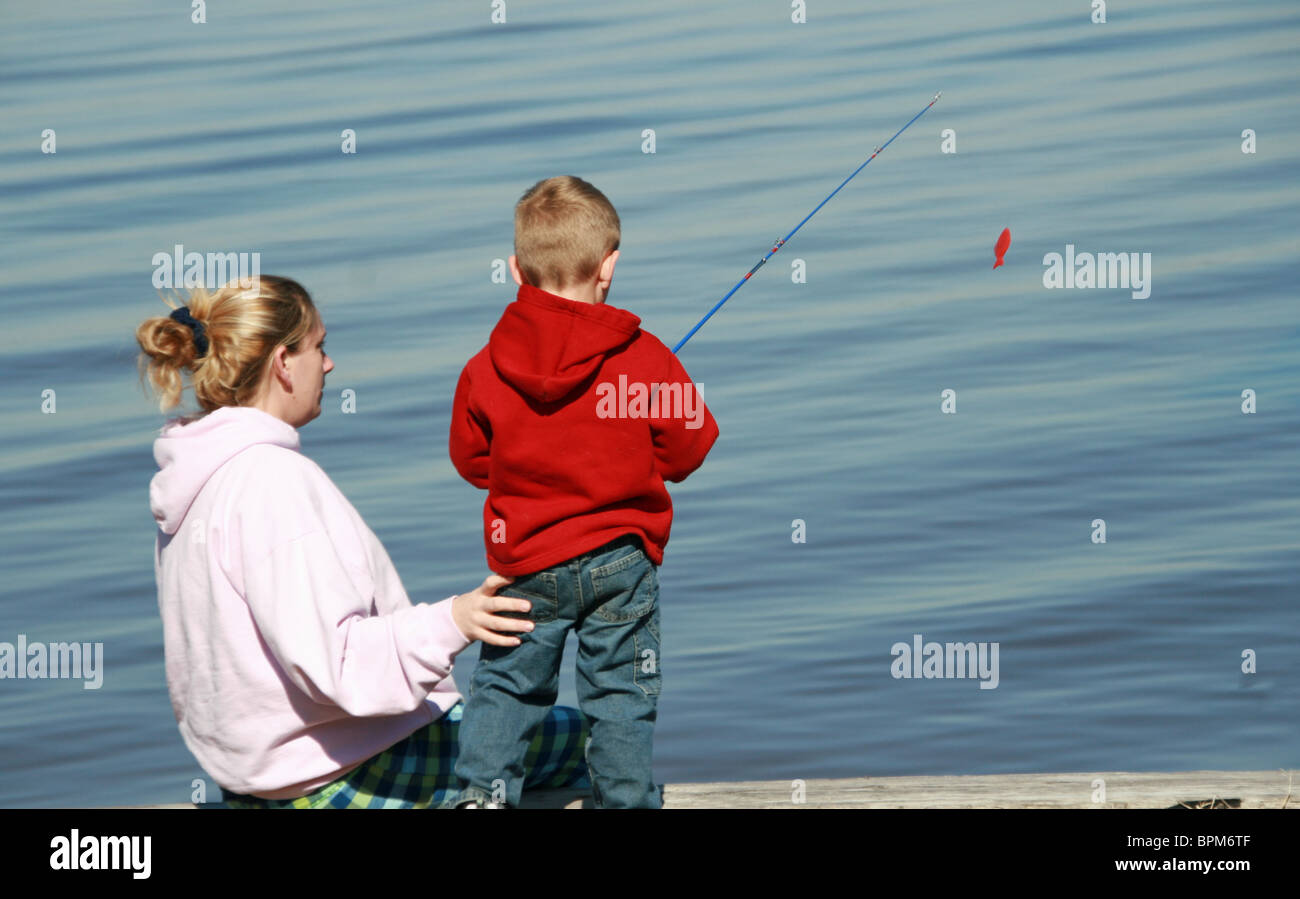 Giovane madre mostra giovane figlio a pescare sul bordo delle acque Foto Stock