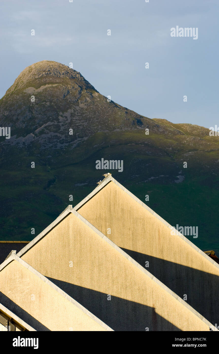 La giustapposizione di picco di montagna del Pap di Glen Coe e il tetto di un hotel la mattina con il sorgere del sole. Foto Stock