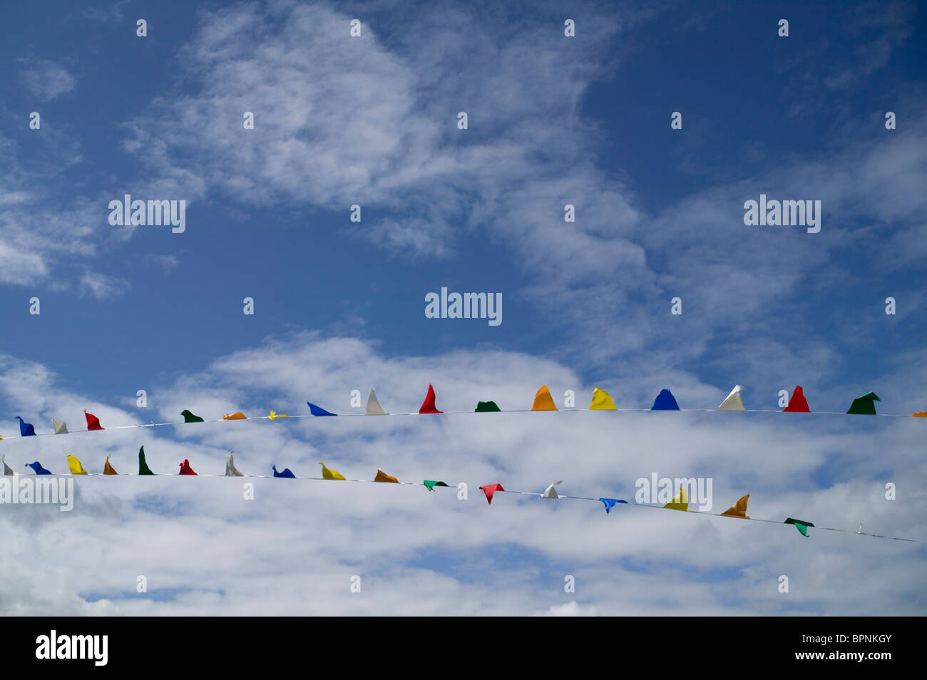 Colorato bunting soffia nella brezza estiva, impostare contro un luminoso cielo blu completo di wispy nuvole bianche. Foto Stock