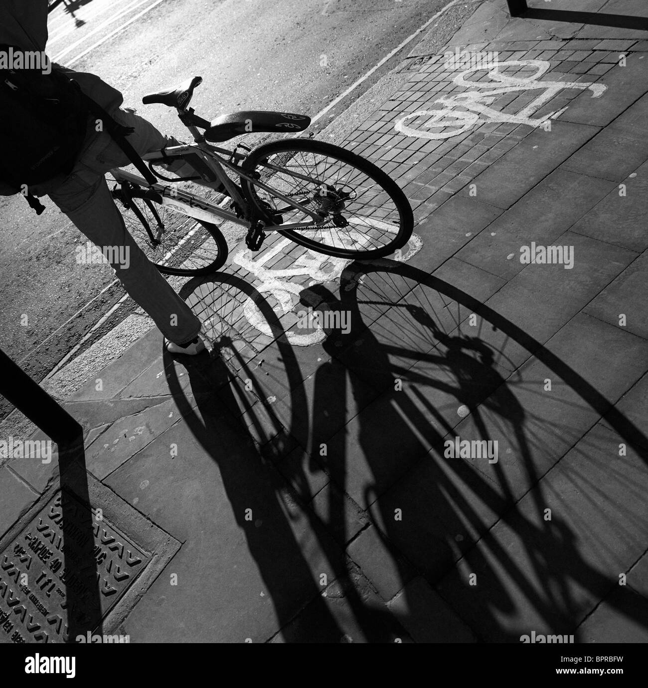 Le ombre di una bicicletta le ruote e il suo pilota sparsi su una pavimentazione di Londra (marciapiede). Foto Stock