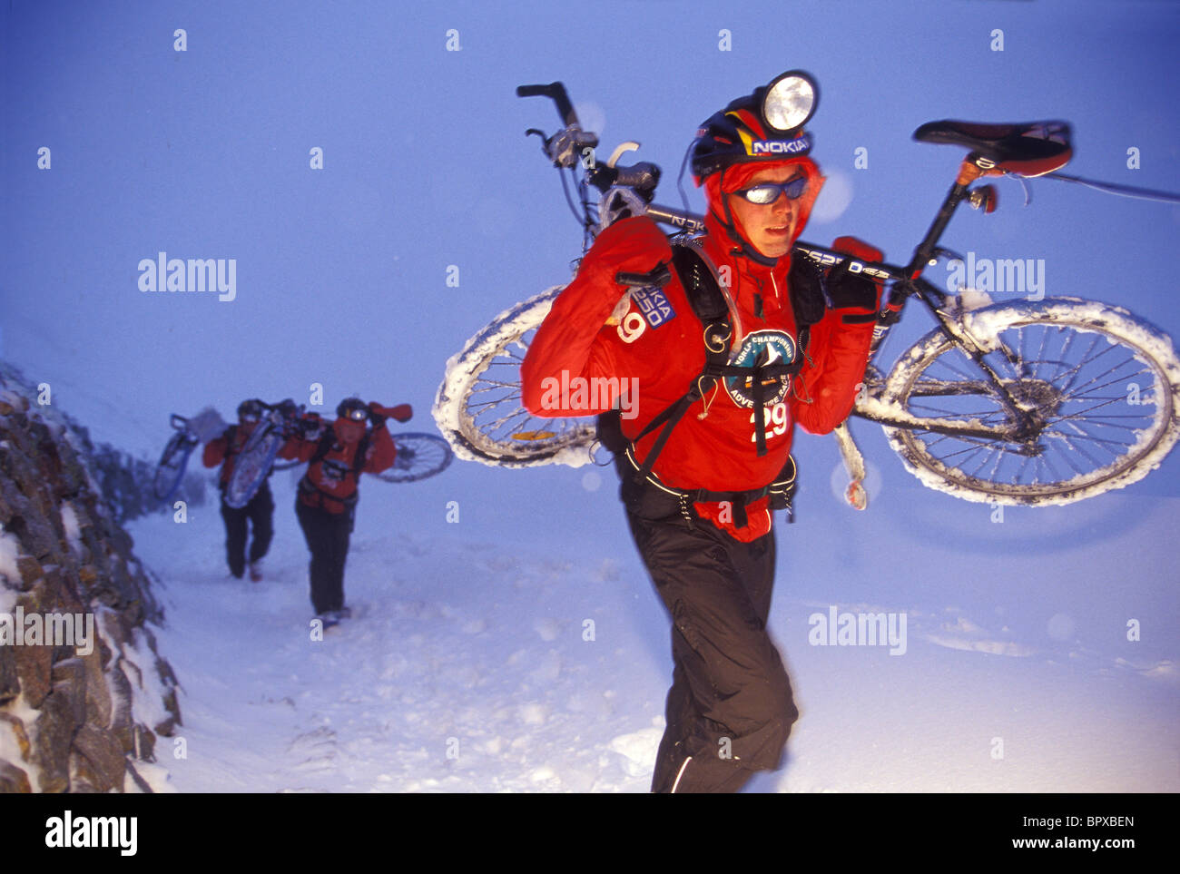 Uomo che porta bici di montagna nella neve durante la gara di avventura in Svizzera (Nokia branding, effetti flash) Foto Stock
