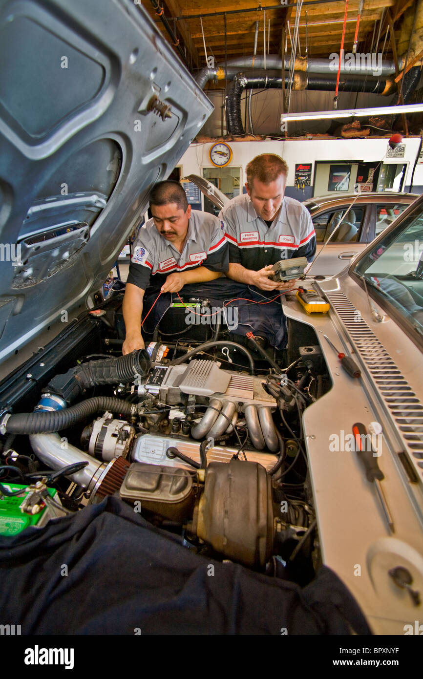 Un ispanico e un meccanico caucasica sintonizzare un motore del camion in un garage indipendente nella California Meridionale. Foto Stock