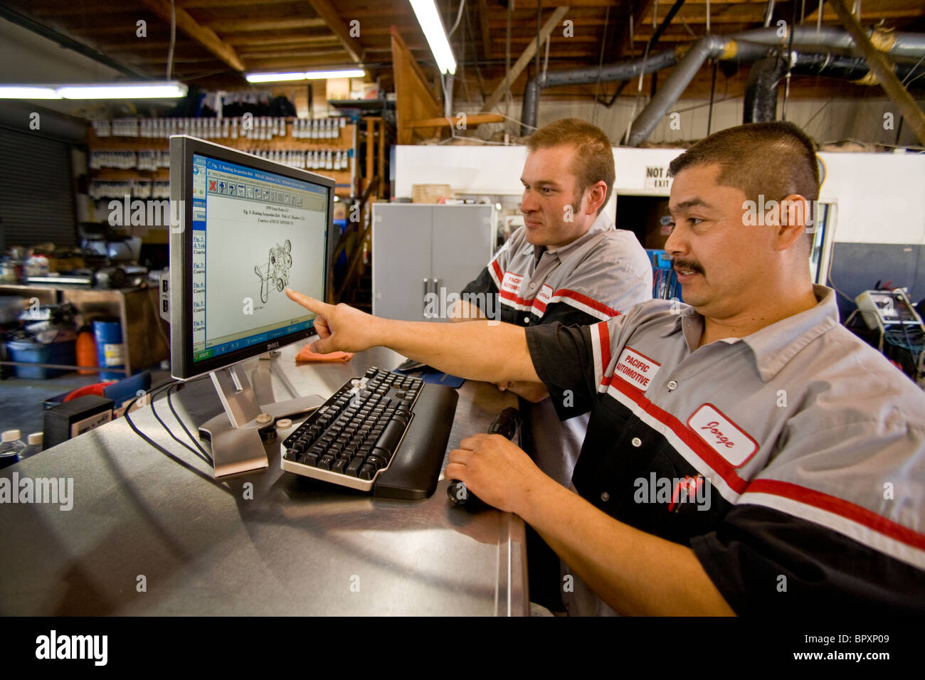 Controllo di una immagine schematica di un motore di automobile sul monitor di un computer, due meccanici in modo indipendente la California del Sud Foto Stock