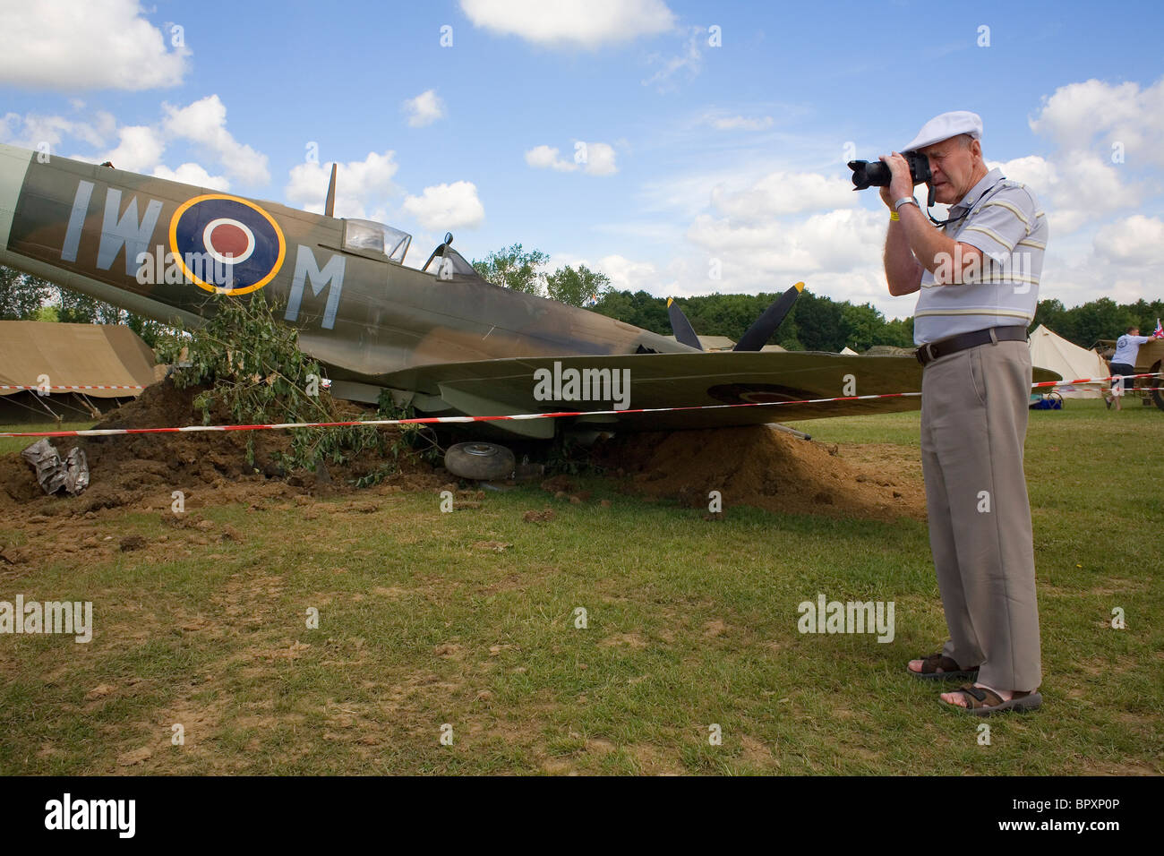 Un uomo in un cappuccio bianco scatta una foto accanto ad un aereo Spitfire. Foto Stock