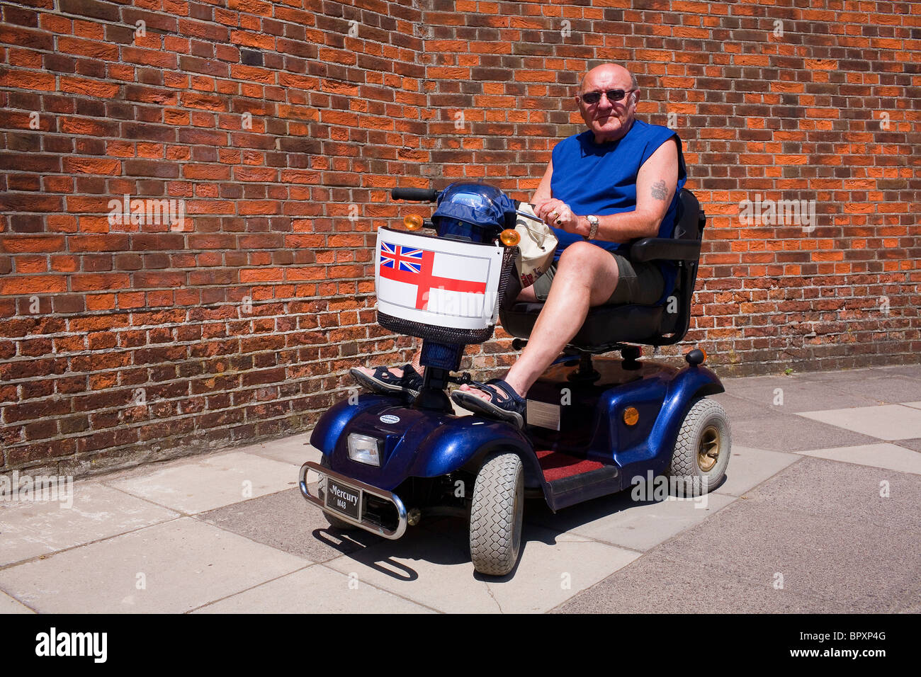 Un vecchio uomo in uno scooter di mobilità con la bandiera di San Giorgio sulla parte anteriore. Foto Stock