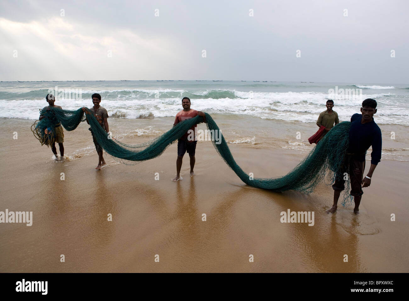 Gruppo di Pescatori indiani sulla spiaggia prendere la rete da pesca dopo lavaggio in mare presso il villaggio di pescatori a Puri. Foto Stock