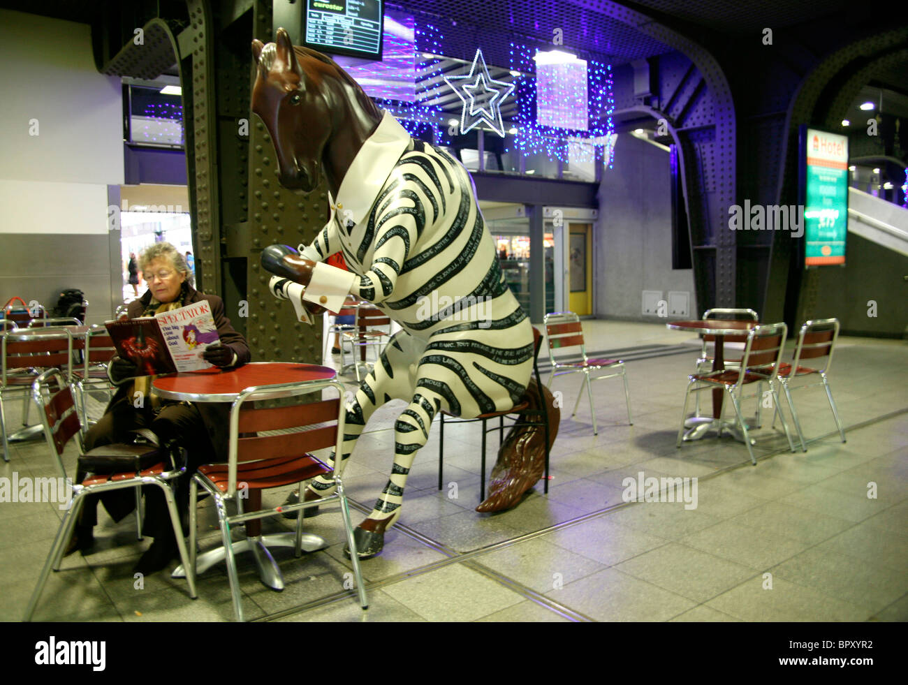 Un cavallo avente un caffè con una donna lettura, cafe tabella a Bruxelles Midi Rail Station, Belgio Foto Stock