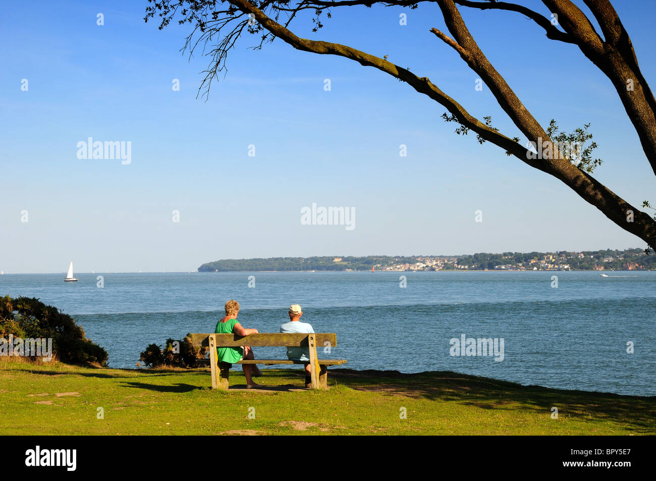Due persone sedute su una panchina che guarda al Solent e all'Isola di Wight dal parco Lepe Country Hampshire England UK Foto Stock