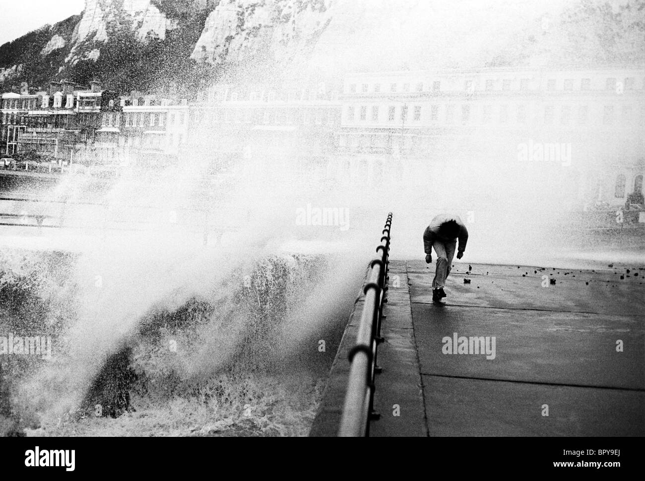L'uomo sul lungomare di Dover anatre sotto storm spruzzare sopra il mare muro di difesa sulla costa sud. Foto Stock