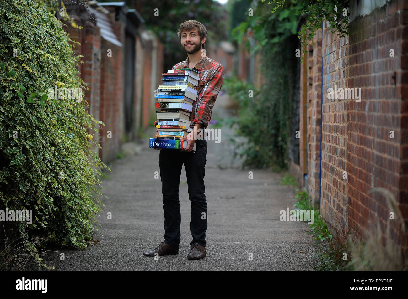 Uno studente in piedi con una grande pila di libri, che illustra lo studio, revisione cramming e revisione Foto Stock