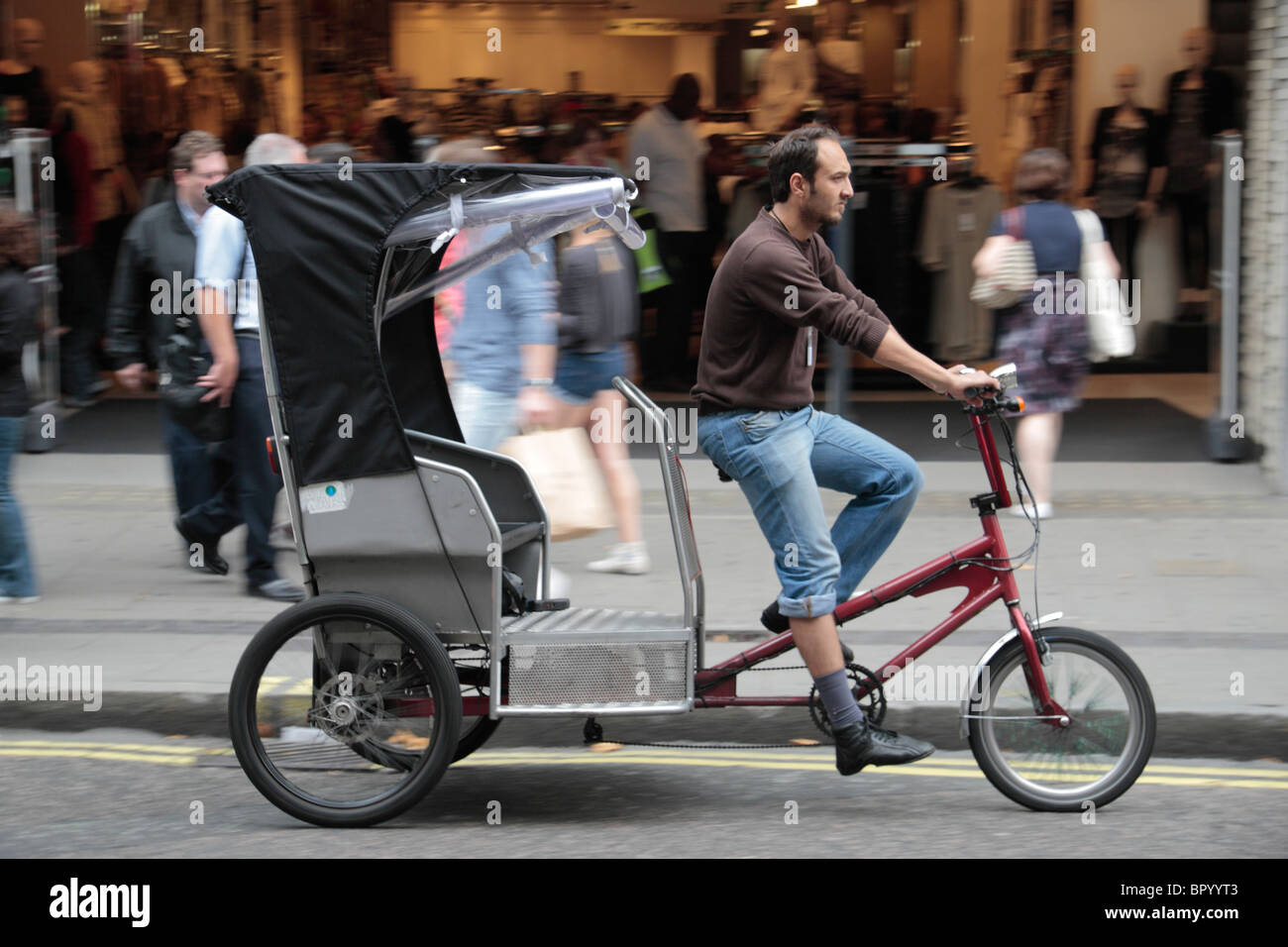 Un pedicab (taxi bicicletta o in rickshaw) spostamento verso il basso di Oxford Street, Londra, Regno Unito. (Deliberata/sfocatura movimento nell'immagine) Foto Stock