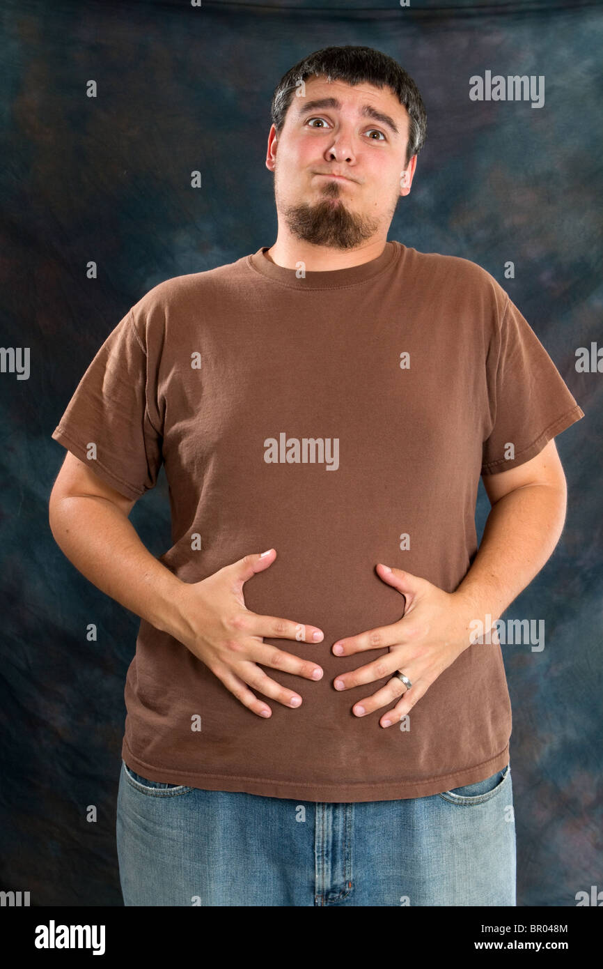 Il sovrappeso uomo tiene il suo stomaco a causa del disagio causato da surriscaldamenti e gonfiore. Foto Stock