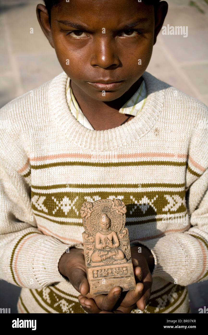 Giovane ragazzo indiano tentare di vendere una piccola statua del Buddha come un prezioso pezzo di storia archeologica ai turisti, Sarnath, India. Foto Stock