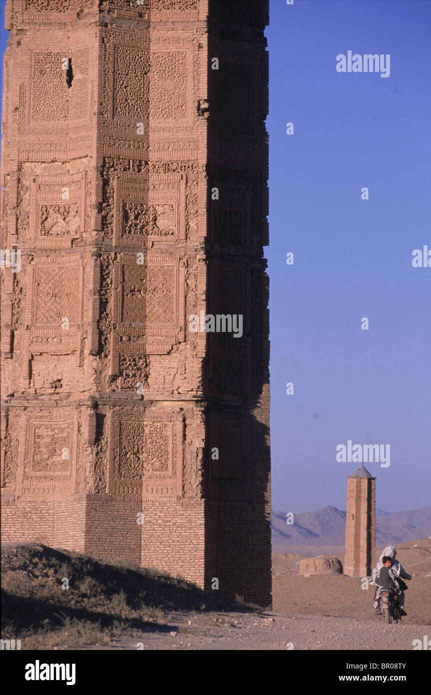 Un uomo in sella a una moto passa un antico minareto al di fuori di Ghazni, Afghanistan. Foto Stock