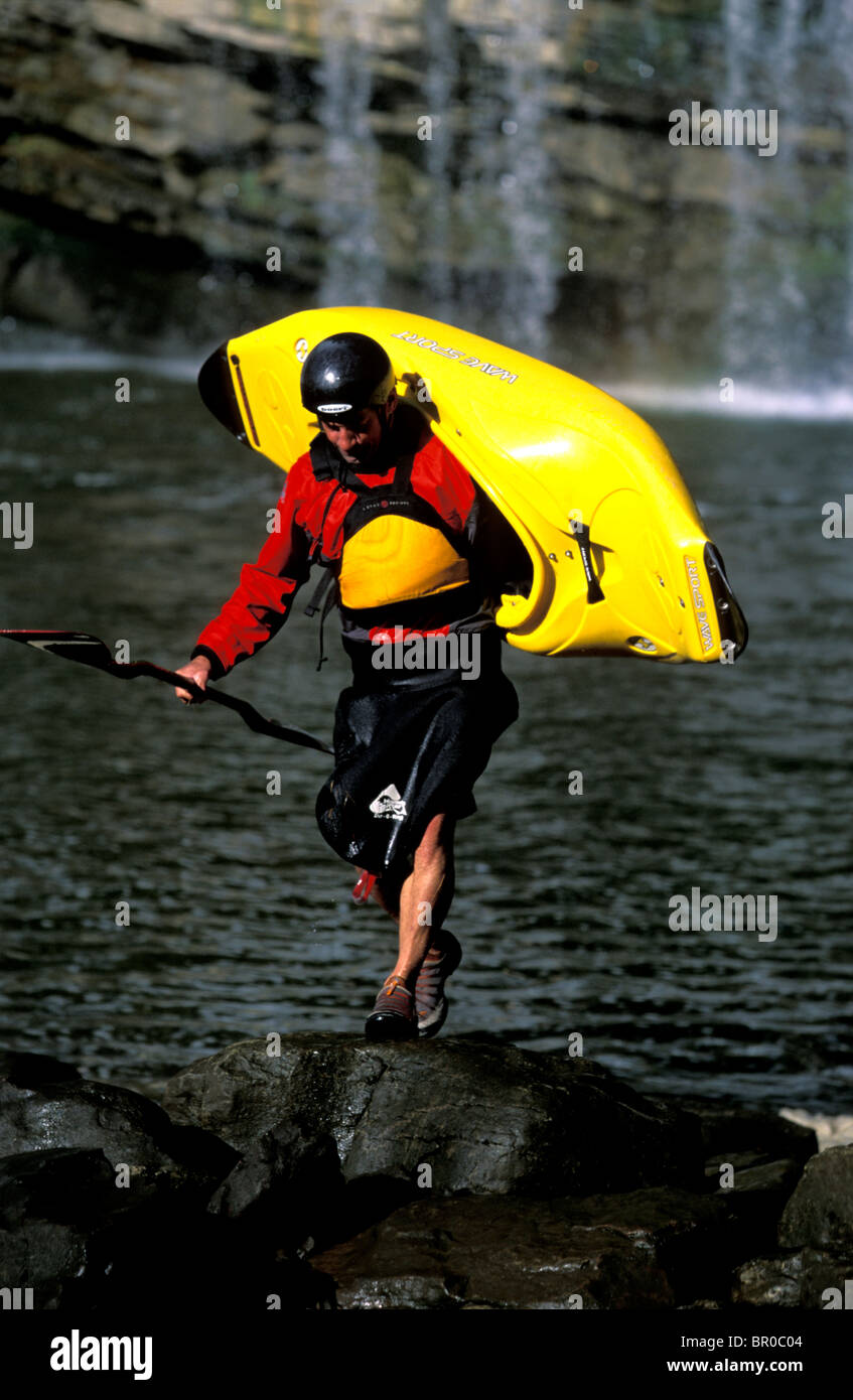 Un uomo che porta il suo kayak accanto a un fiume. Foto Stock